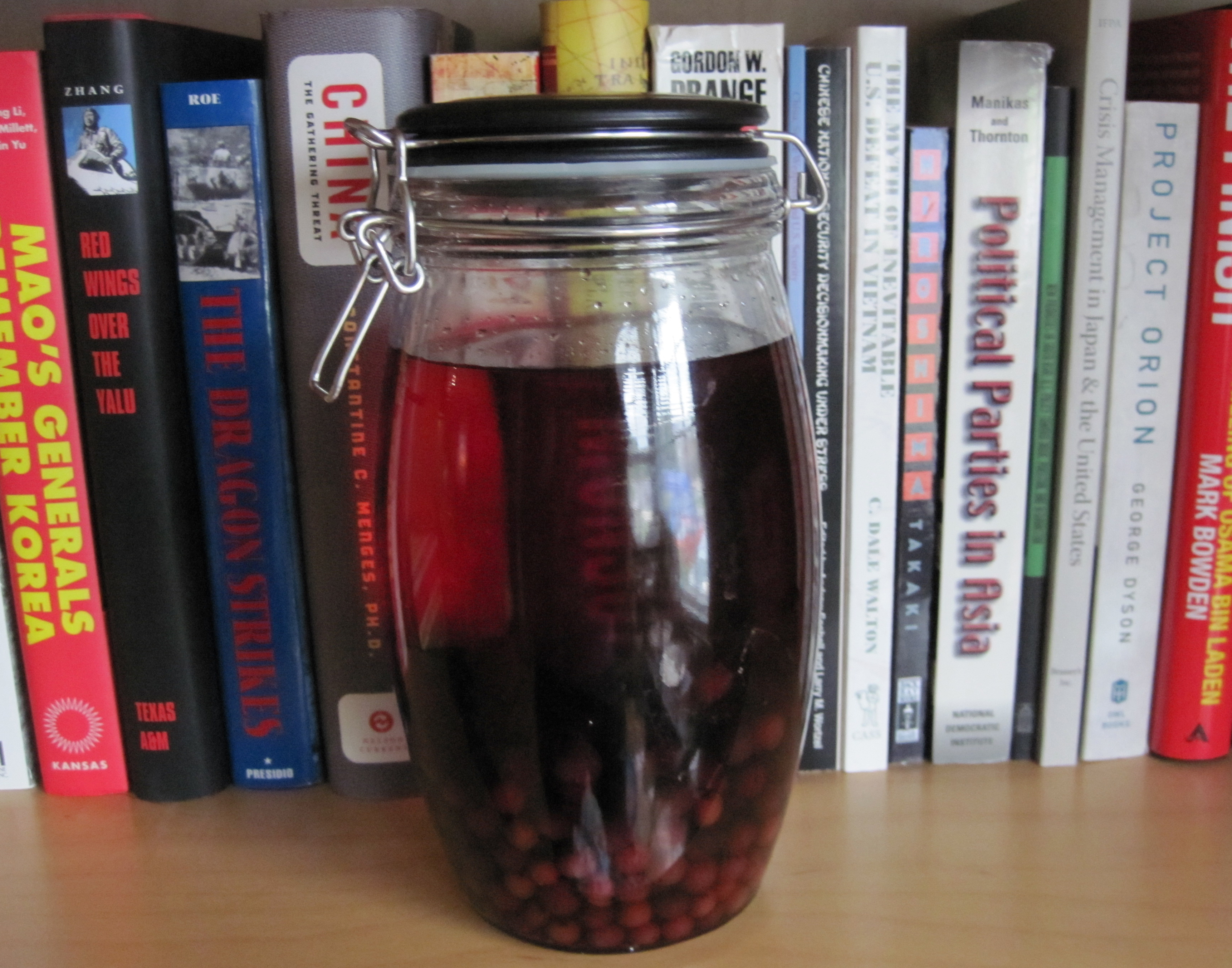 Jar full of berries and red liquid in front of books